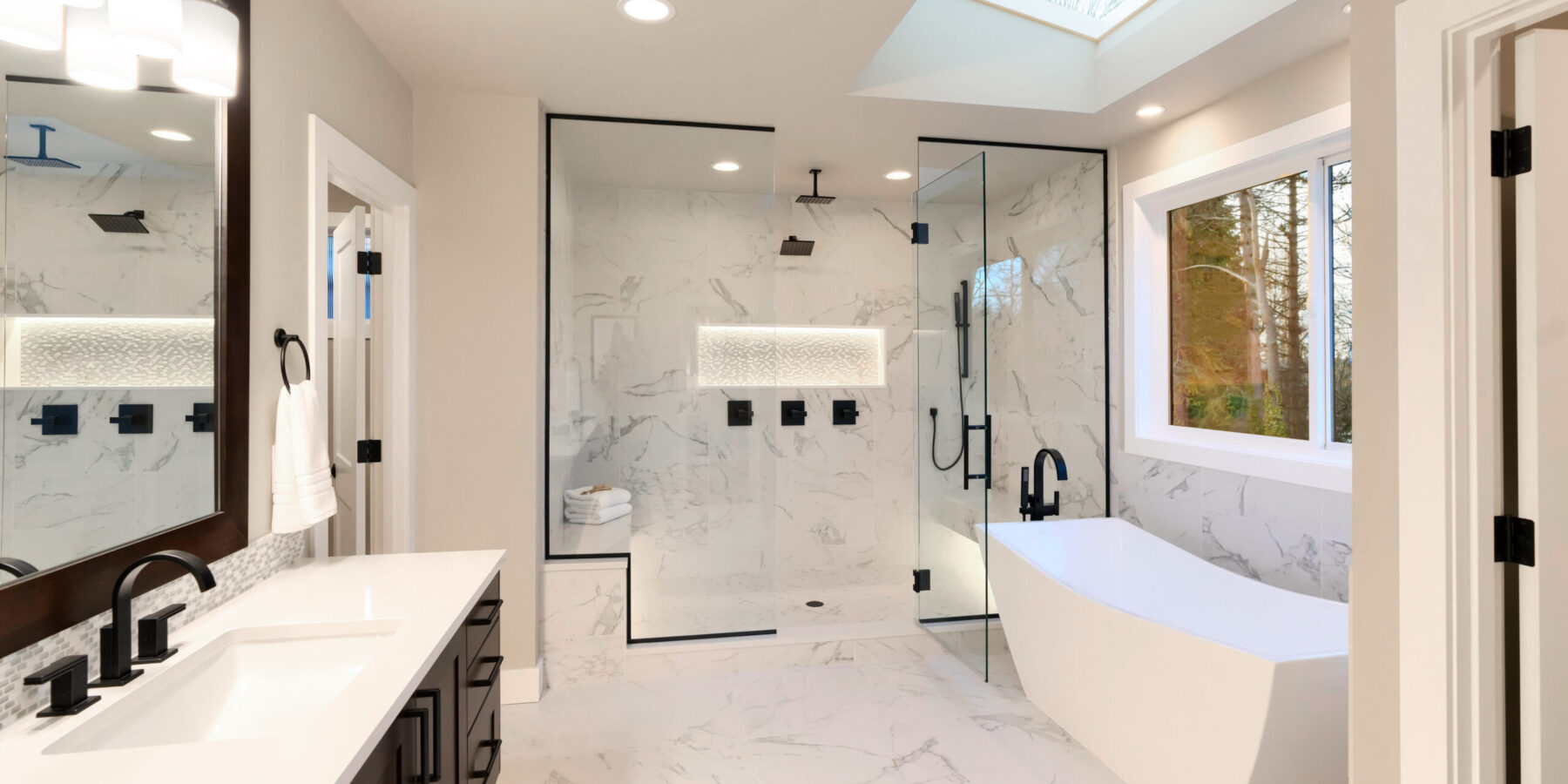 Luxury modern home bathroom interior with dark brown cabinets, white marble, walk in shower, free standing tub, two mirrors, flowers.